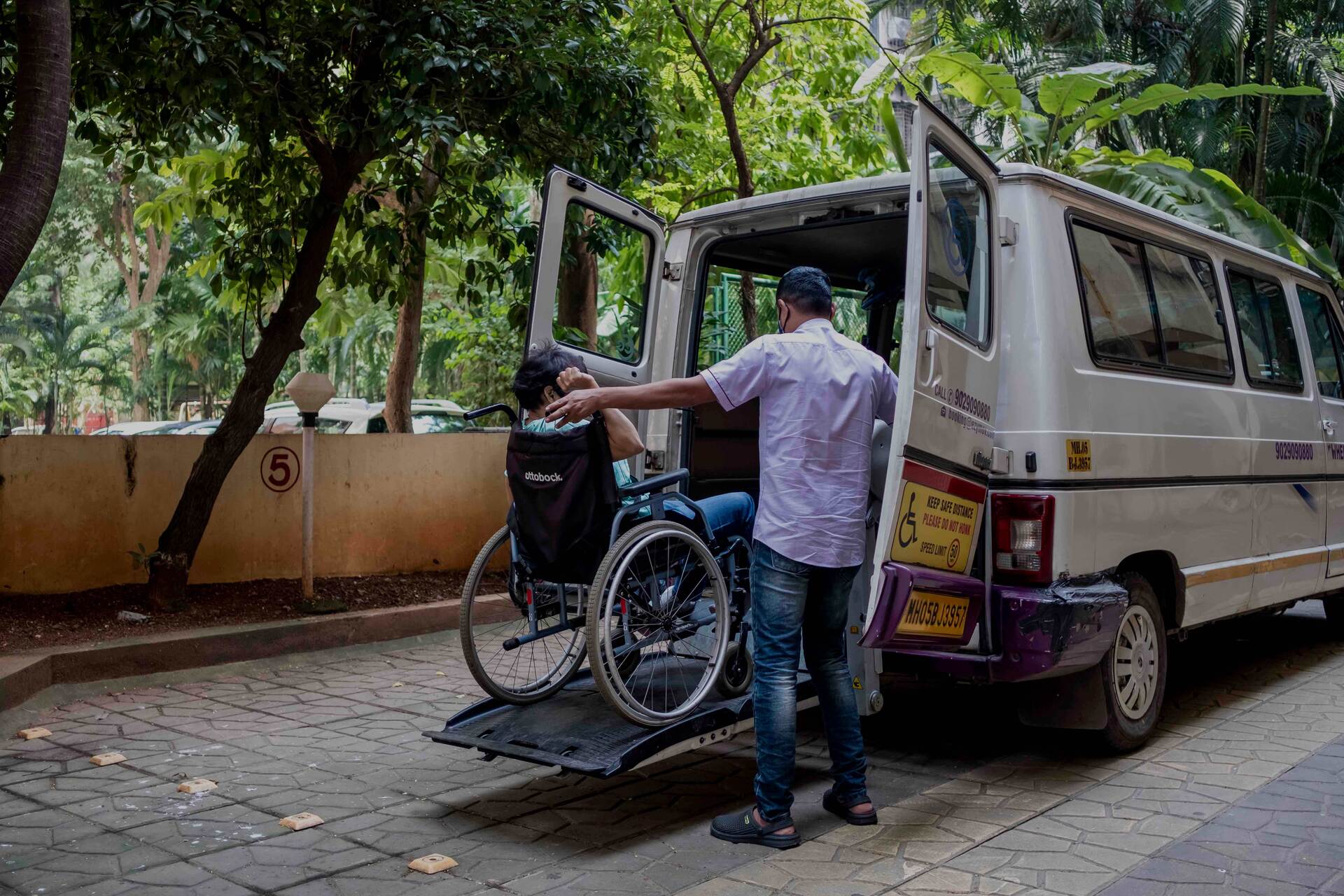 A man uses a lift to help a person in a wheelchair into a taxi van.
