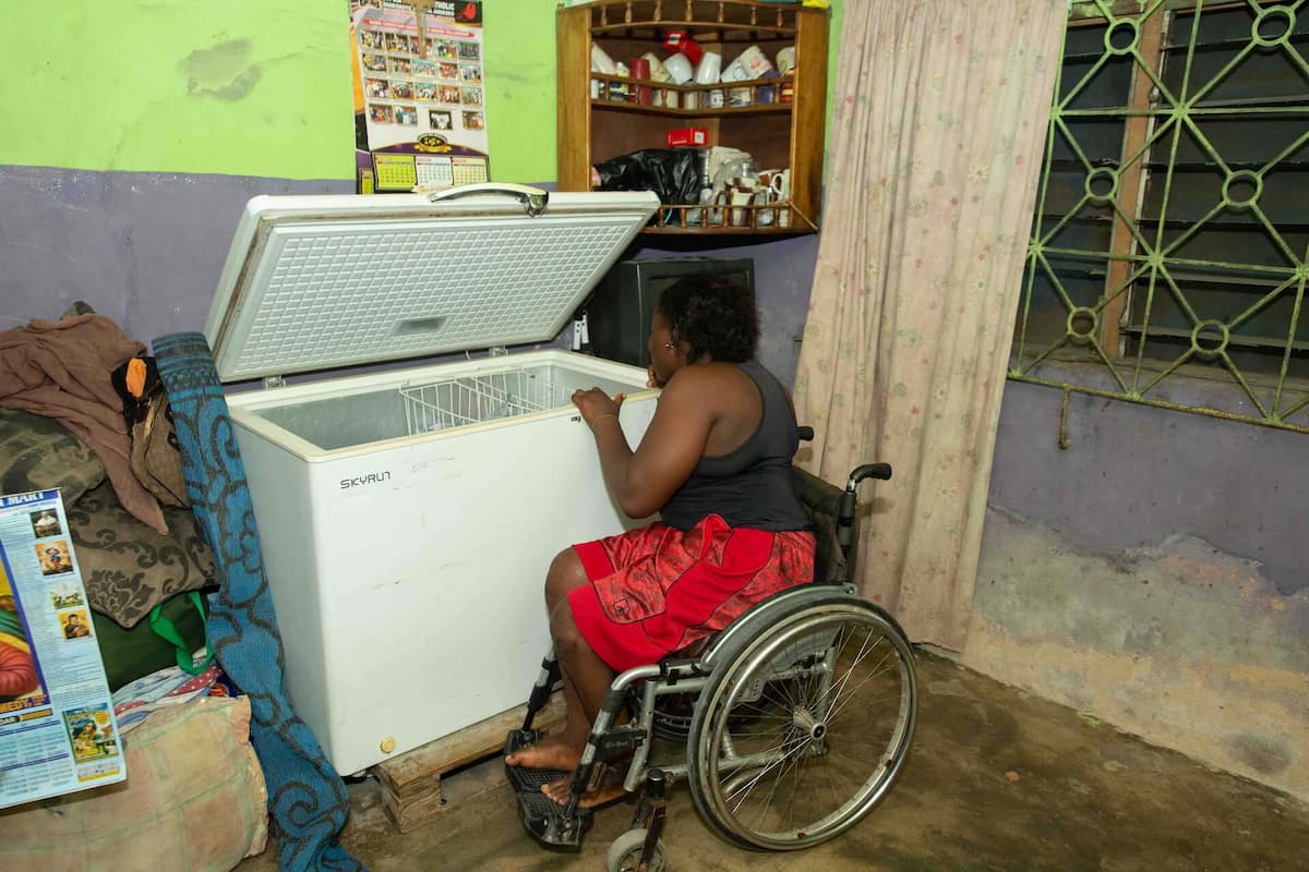 Olajumoke peers over the edge of a chest freezer from her wheelchair.