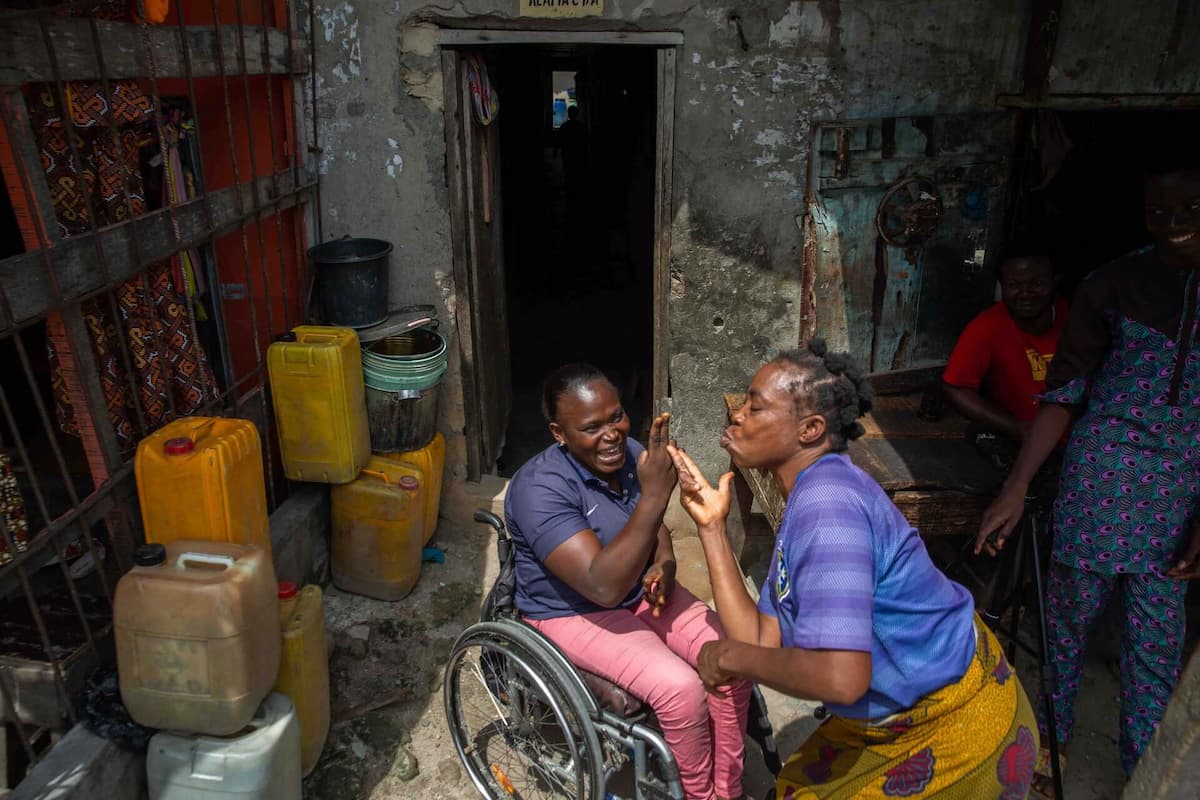 Olajumoke sits in her wheelchair at home laughing with a friend.
