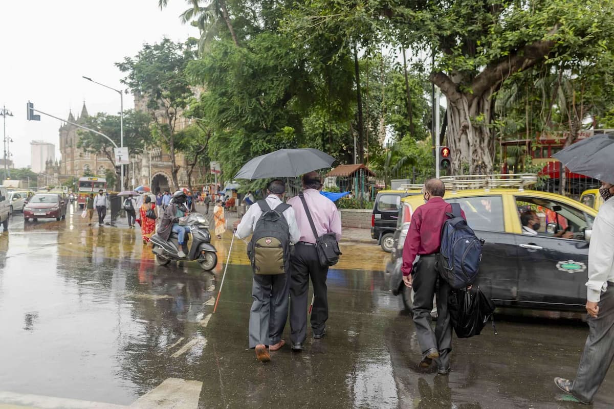 A visually impaired man is escorted across a busy street in the rain, near the historic railway station, formerly known as Victoria Terminus.