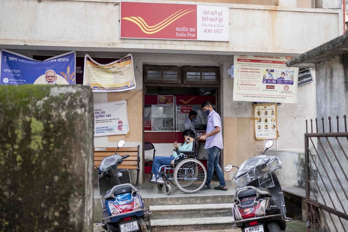 A woman in a wheelchair sits with her caregiver at the top of a flight of steps outside the India Post Office.