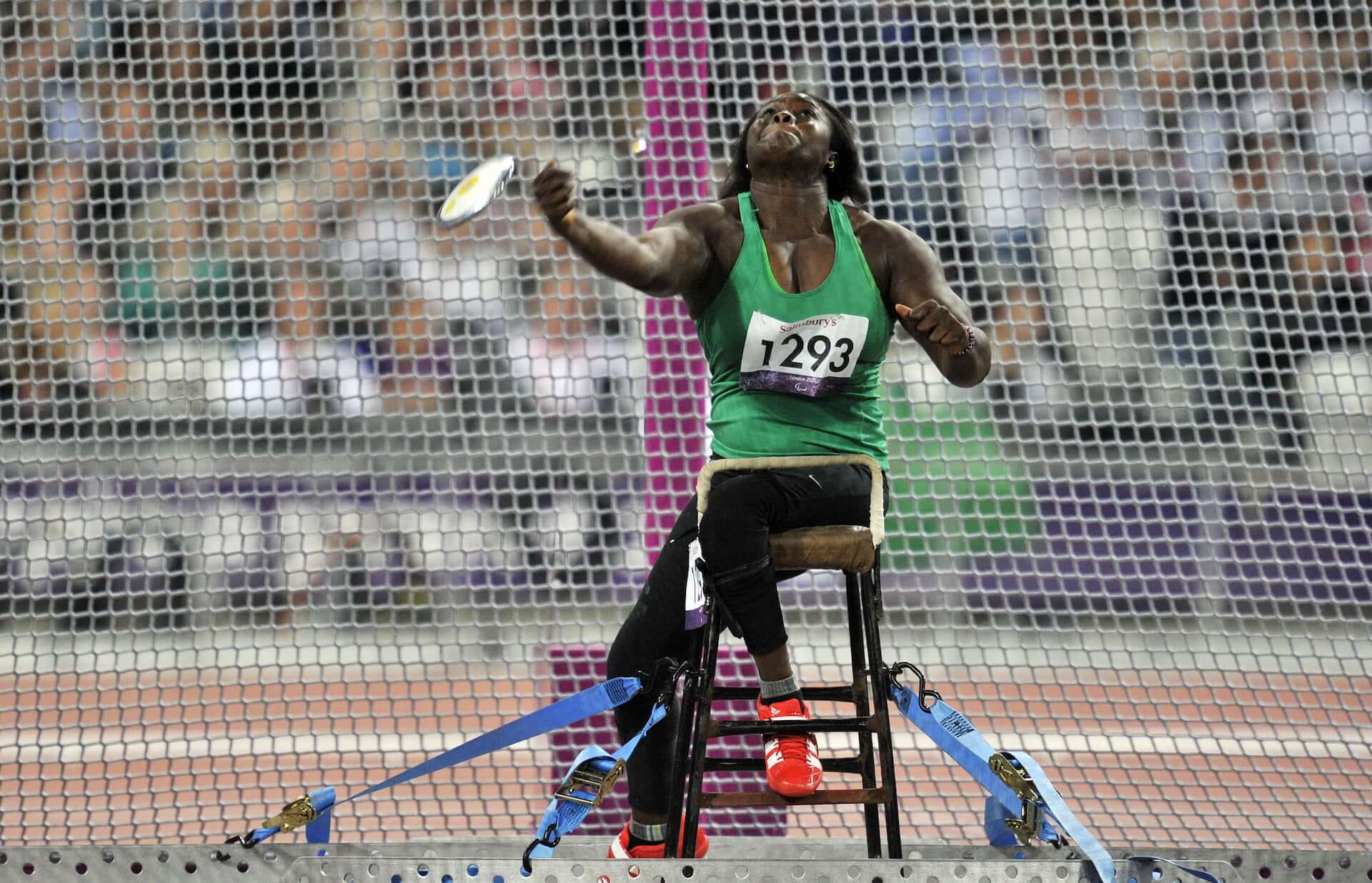 A Nigerian Paralympic discus athlete sits on a stool throwing a discus.