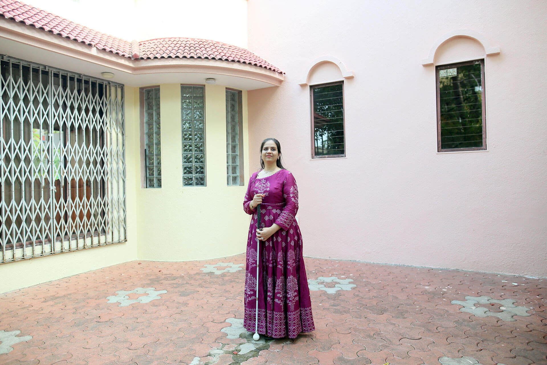 Nidhi, a 36-year-old woman, poses for the camera holding a white cane outside a building in Mumbai, India.