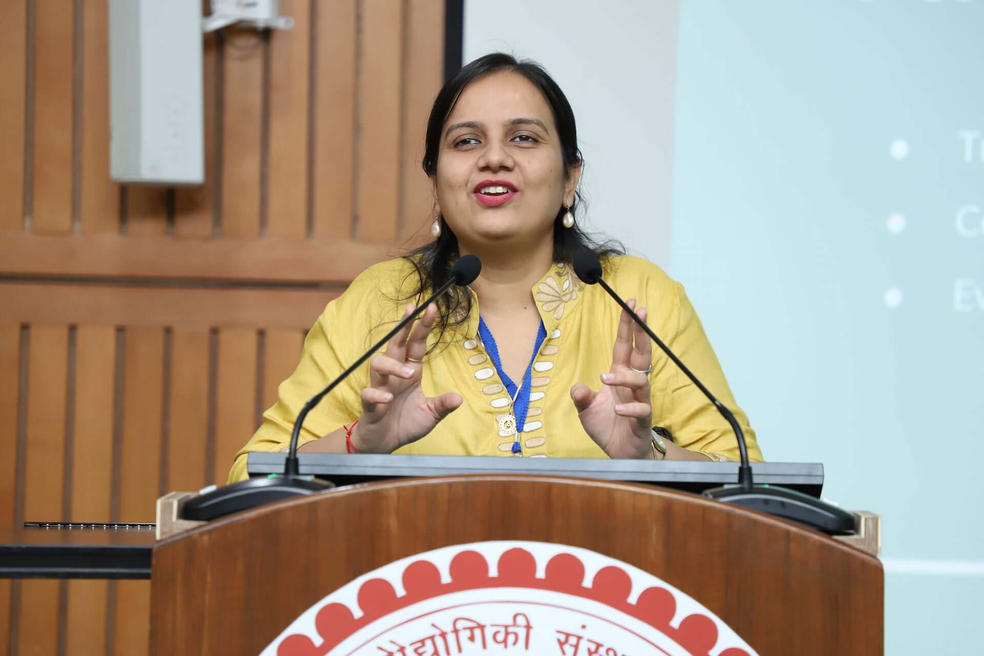 Nidhi stands at a podium speaking at an event.