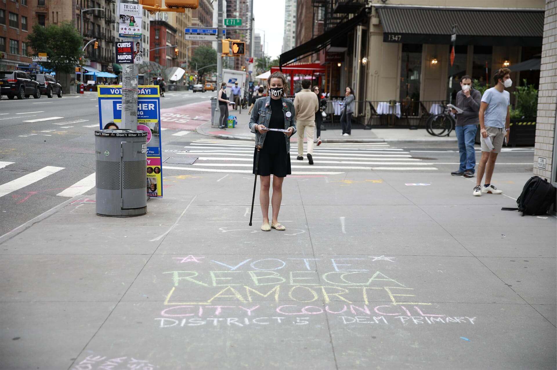 Rebecca poses in front of a pavement chalk message that reads: Vote Rebecca Lamorte, City Council District 5, Dem Primary.