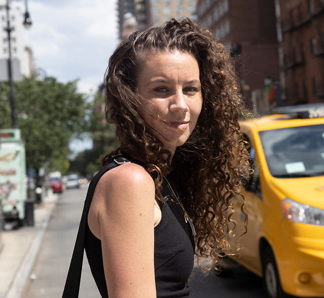 Rebecca, a 30-year-old white woman with long curly hair, poses for a photo in the streets of New York City, US.